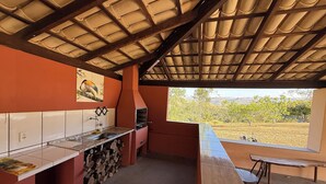 Een keuken met een betegelde achterwand, een hangende pannendroger en uitzicht op een wijngaard door een raam.