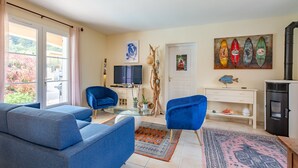 A living room with a sofa, chairs, a TV, a fireplace, and a painting of surfboards.