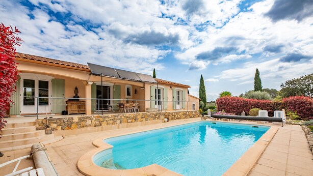 A house with a swimming pool, a patio with chairs, and a stone wall.