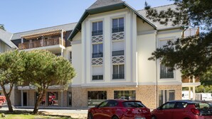 A multi-story building with a modern architectural style, featuring a prominent entrance with a glass door and a balcony with a lattice design.
