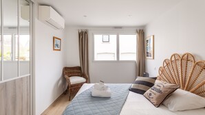 A bedroom with a bed, a wicker chair, a window, and an air conditioning unit.