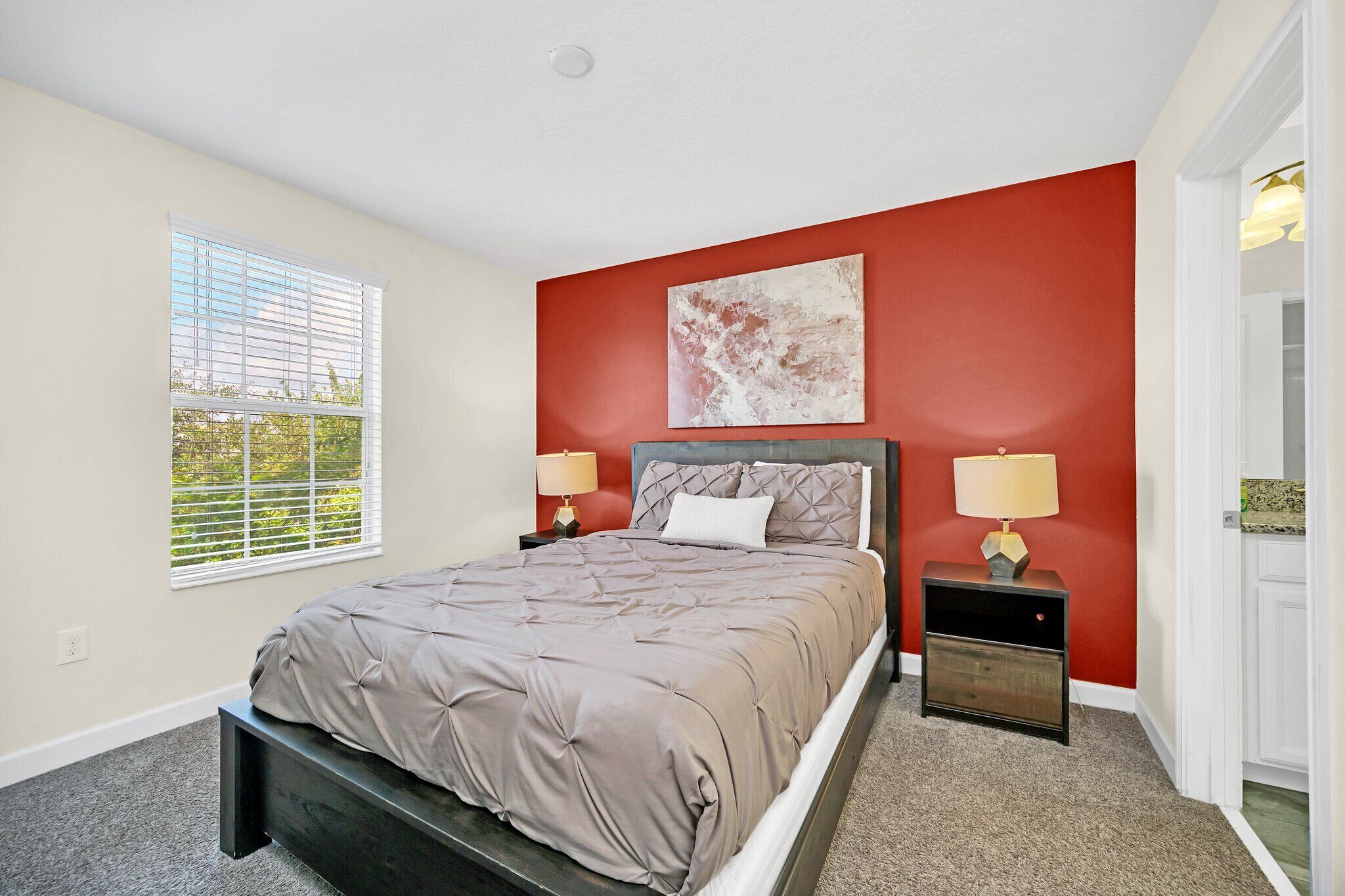 A bedroom with a bed, two bedside tables, a window, and a red accent wall.