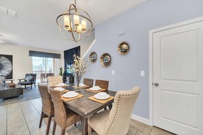 Un comedor con una mesa de madera oscura dispuesta para cuatro personas, rodeado de sillas de mimbre y una butaca tapizada en tono crema.
