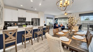 A modern kitchen with white cabinets, a central island, and a dining area with a wooden table set for six. - Last Minute Disney Getaway! Townhouse with Private Pool. Book Now! #124379 (Orlando)
