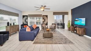A modern living room with a blue sofa, wooden coffee table, and a ceiling fan. - Last Minute Disney Getaway! Townhouse with Private Pool. Book Now! #124379 (Orlando)