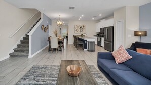 A modern living room with a blue sofa, wooden coffee table, and a staircase leading to another level. - Last Minute Disney Getaway! Townhouse with Private Pool. Book Now! #124379 (Orlando)