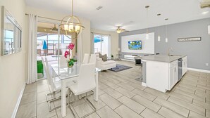 Un vaste espace de vie comprenant une table à manger, des canapés blancs, un îlot de cuisine et un ventilateur de plafond.