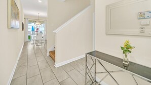 Un intérieur moderne avec un escalier, une table en verre ornée d’un vase et un tableau encadré accroché au mur.