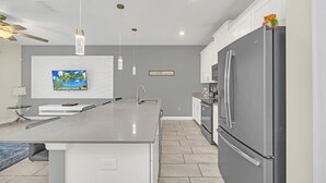 Une cuisine moderne dotée d’un grand îlot central, d’appareils électroménagers en acier inoxydable, d’un éclairage suspendu et d’un îlot de cuisine intégrant un évier.