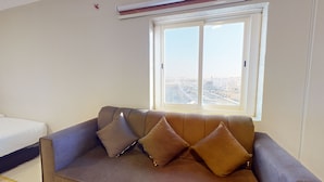 A living room with a sofa, two pillows, and a window with a city view. - Hotel Al Madinah Hotel Apartments (Madinah)