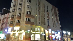 A multi-story hotel with balconies, a ground floor with shops, and illuminated signage. - Hotel Al Madinah Hotel Apartments (Madinah)