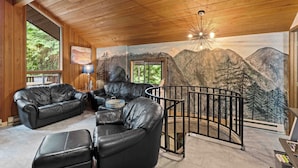 Un interior de madera con un mural de montañas, sofás de cuero y una escalera.