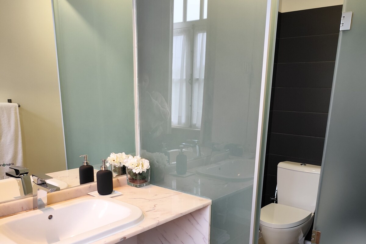 A modern bathroom with a marble sink, a glass shower enclosure, and a toilet.