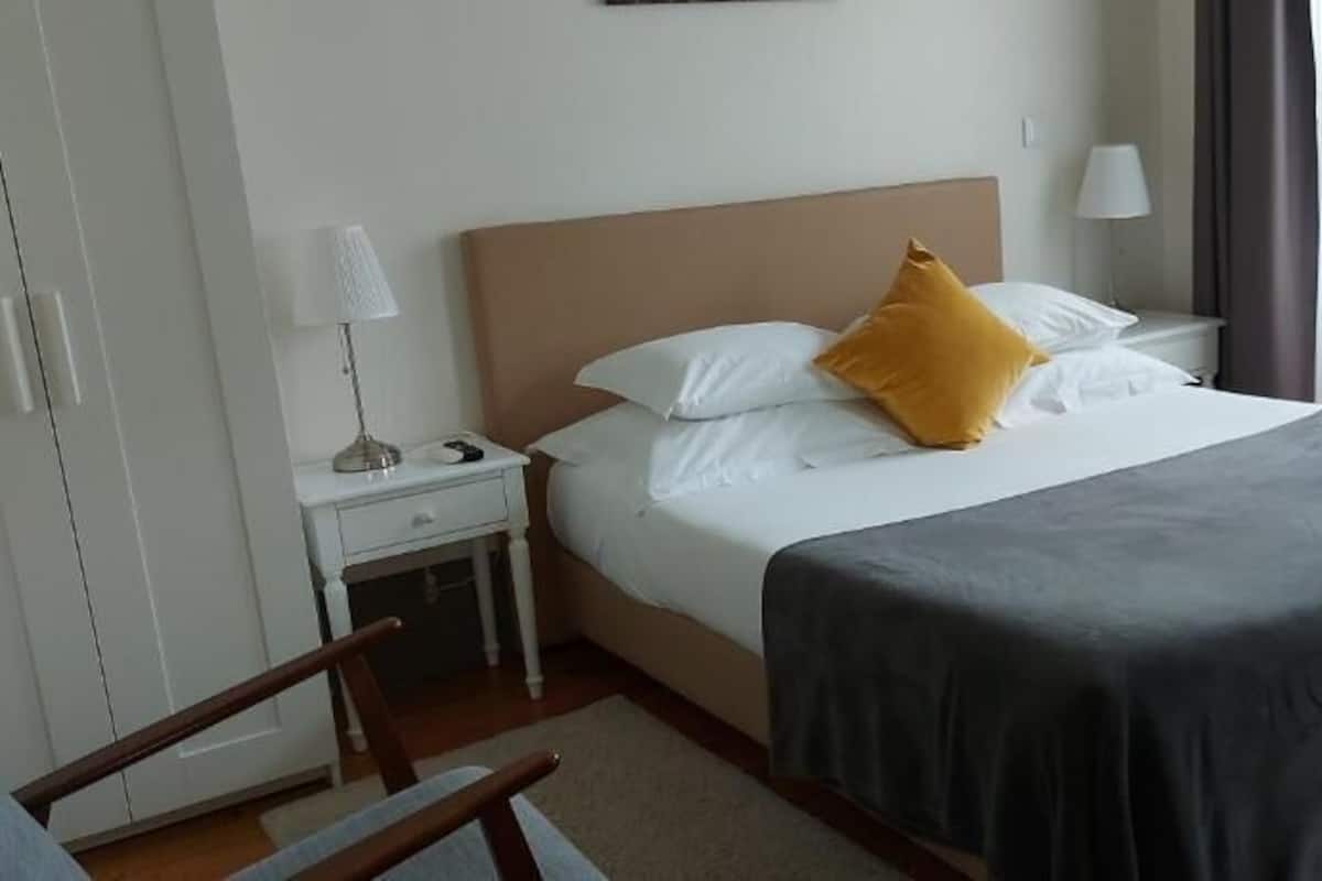 A hotel room with a bed, a nightstand, a lamp, a chair, and a wardrobe.