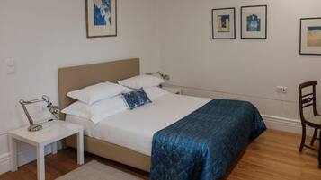 Un dormitorio con cama, mesita de noche, lámpara y una obra de arte en la pared.