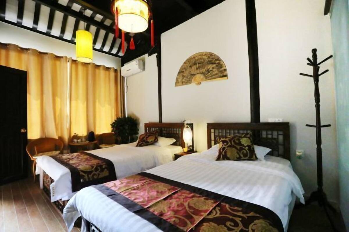 A hotel room with two beds, a wooden headboard, a traditional fan, and a coat rack.