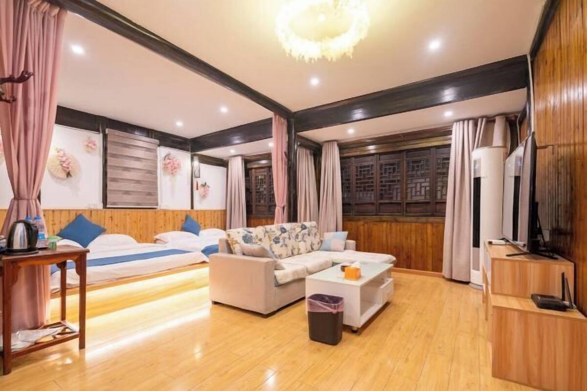 A hotel room with a sofa, a small table, a TV, and a wooden floor.