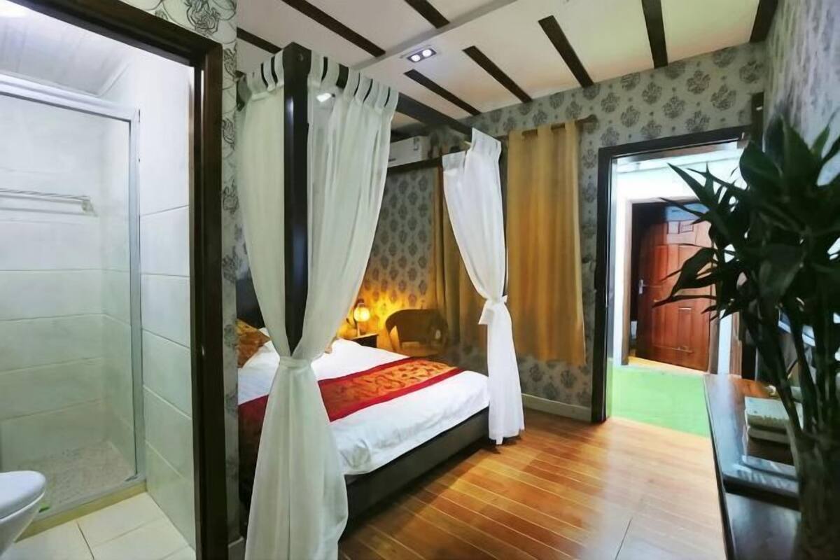A bedroom with a bed, a bedside table, a chair, a curtain, and a door.