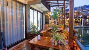 A wooden deck with a table and chairs, surrounded by potted plants, overlooking a water body and traditional buildings. - Zhouzhuang Qingfeng Mingyuelou Boutique Inn (Kunshan)