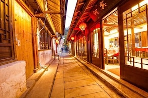 Um beco estreito com edifícios de madeira tradicionais, um banco e uma mesa com cadeiras em frente a um restaurante.
