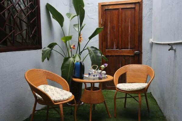 Un pequeño espacio al aire libre con sillas de mimbre, una mesa, una planta en maceta y una puerta de madera.