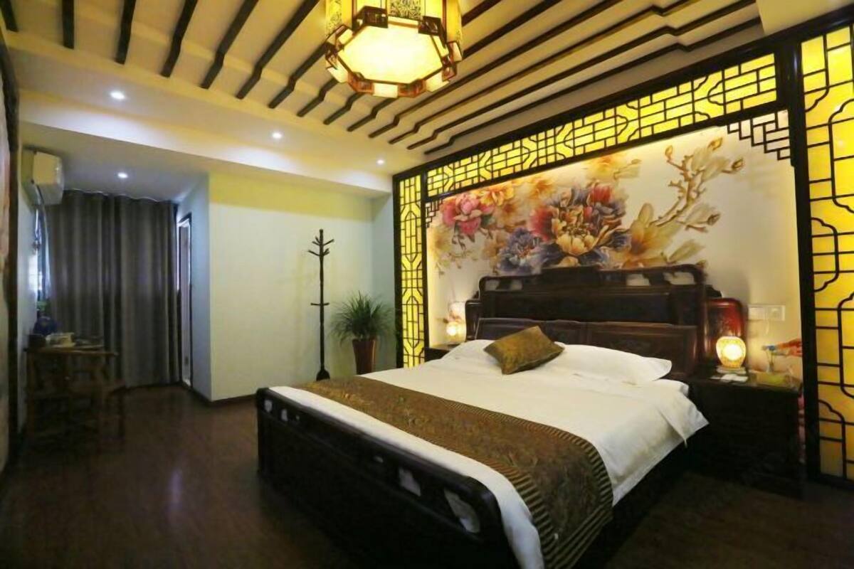 A bedroom with a bed, a nightstand, a lamp, a potted plant, and a decorative wall panel.