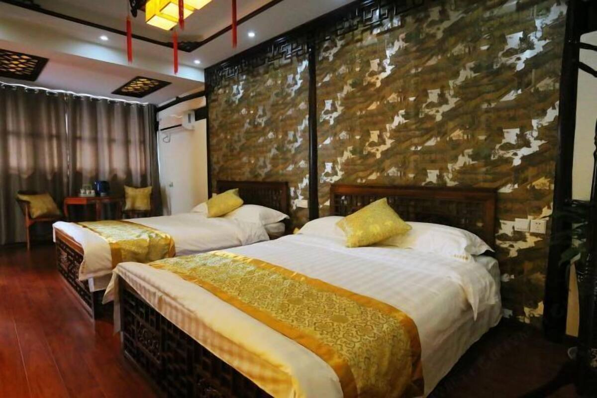 A hotel room with two beds, wooden headboards, a curtain, and a patterned wall.