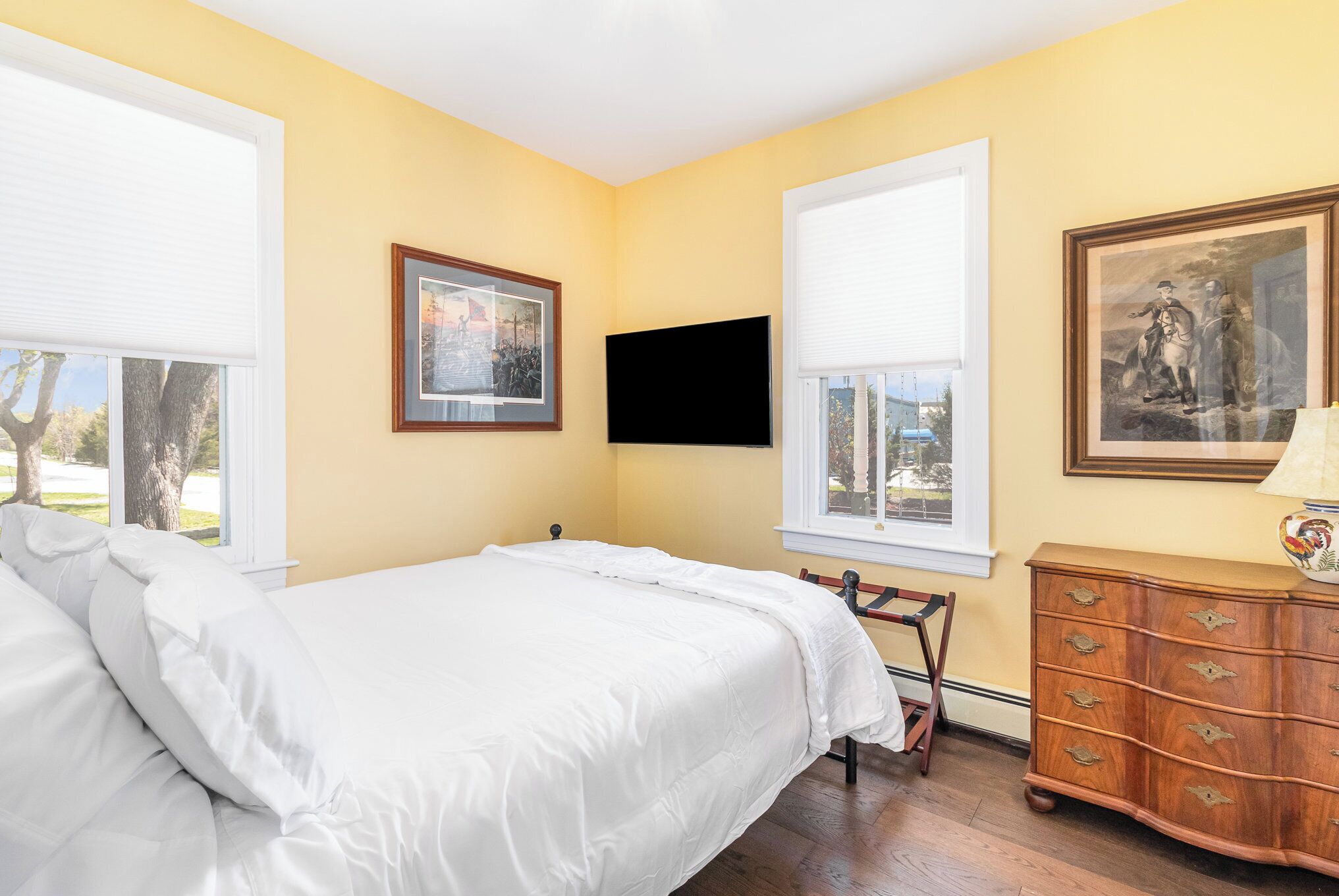 Une chambre à coucher avec un lit, une commode, un téléviseur et deux fenêtres.