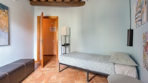 A compact room with a bed, a bench, and a table. There is a door leading to another room. - Vigna Nuova Third Floor (Firenze)