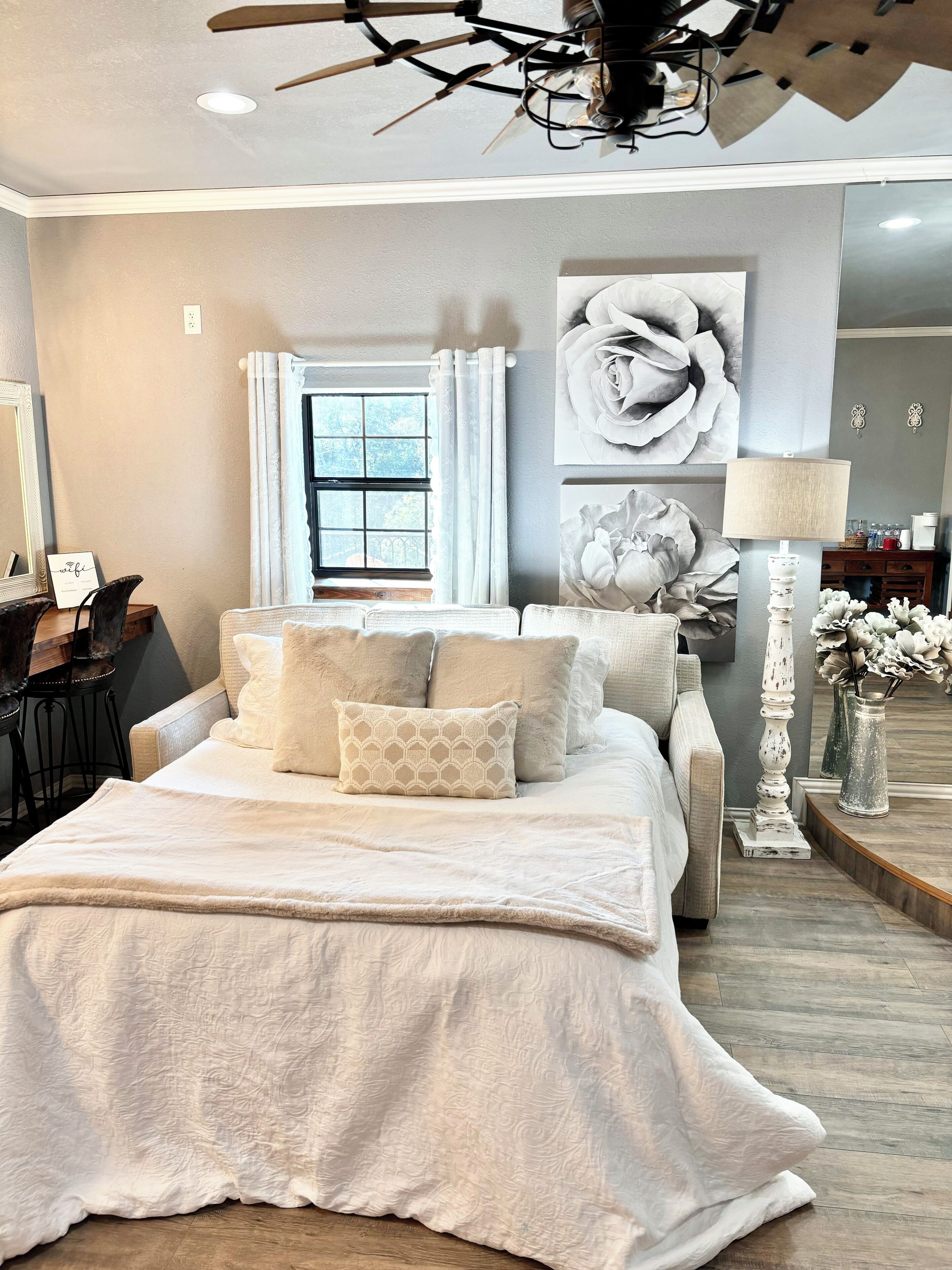 A bedroom with a large bed, a ceiling fan, a window with curtains, and a desk with a chair.