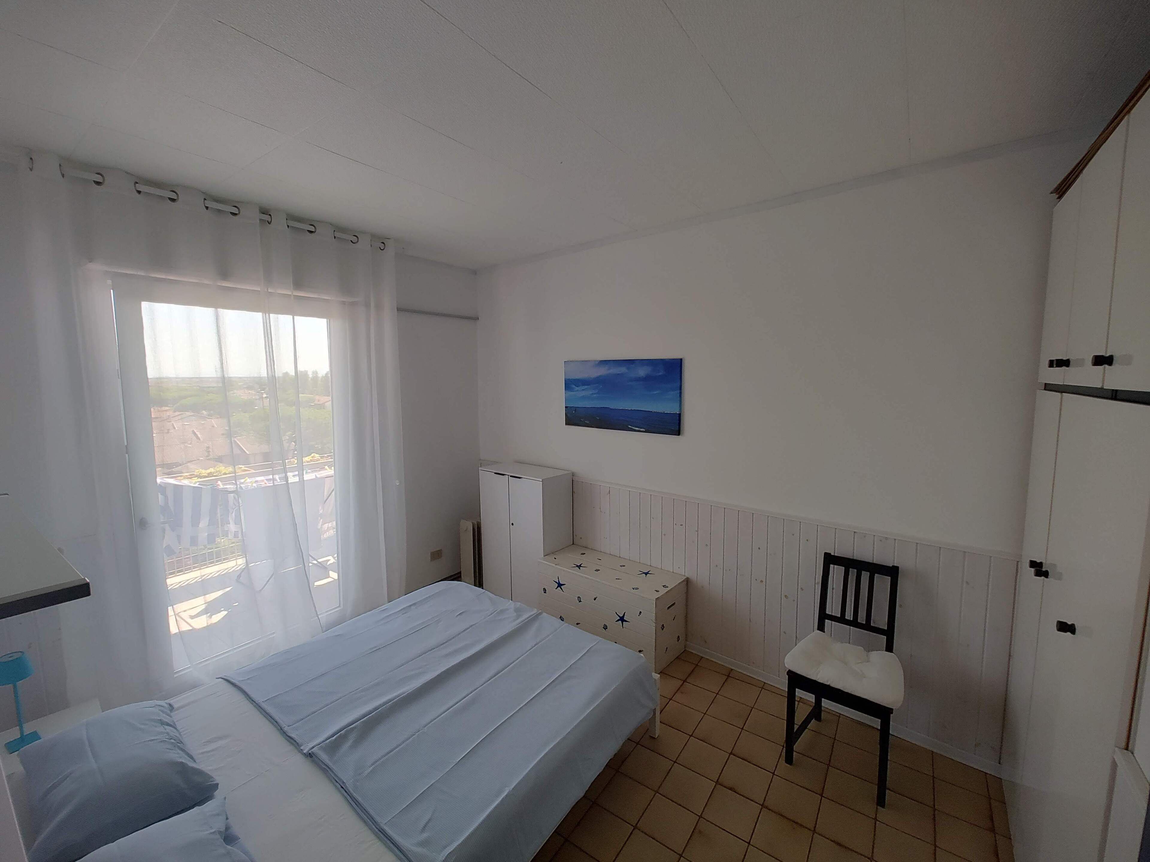 A bedroom with a bed, a chair, a radiator, a wardrobe, and a painting on the wall.