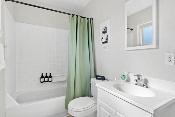 A bathroom with a bathtub, toilet, and sink. There are toiletries on the wall and a green shower curtain.