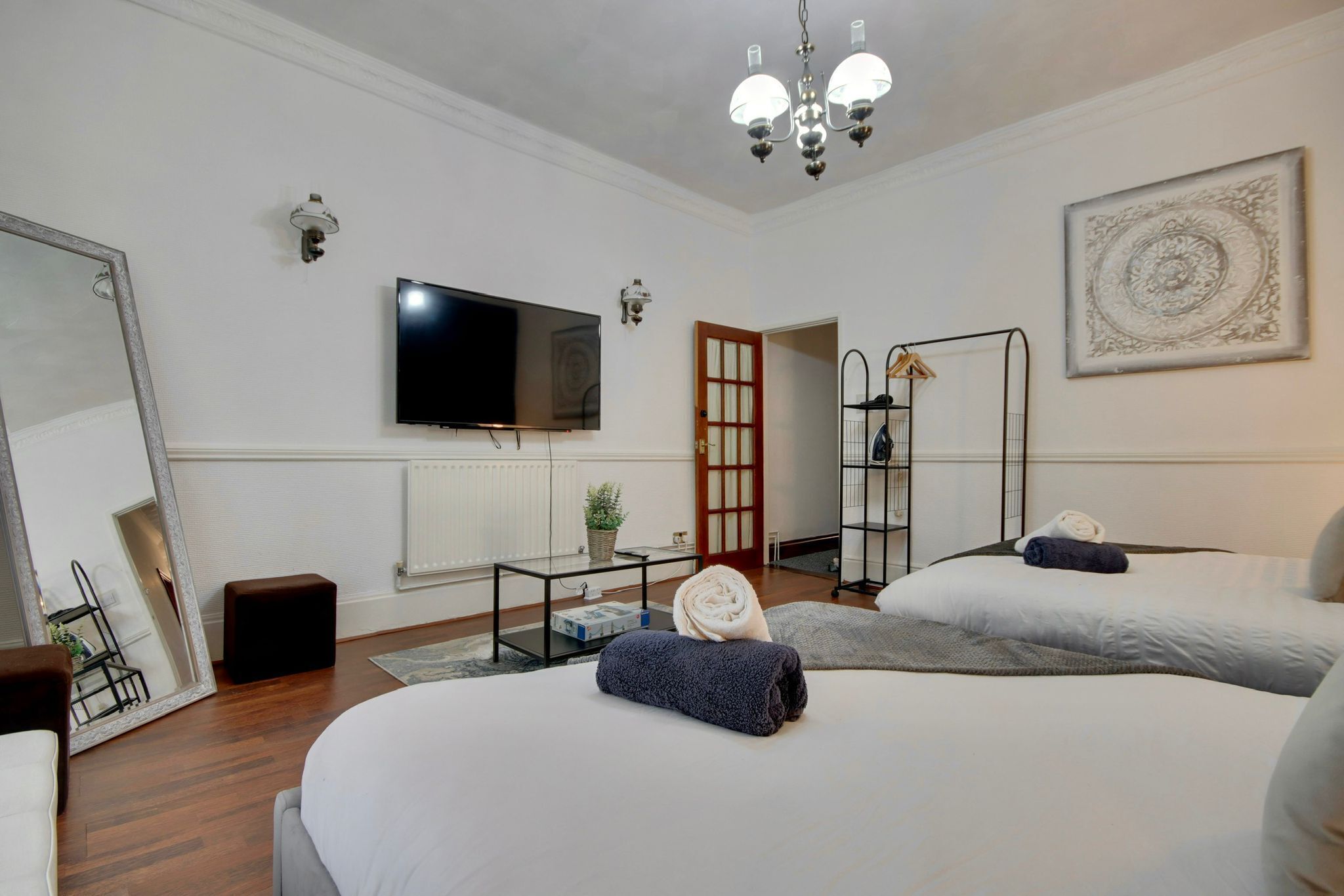 Een hotelkamer met twee bedden, een flatscreen televisie, een kroonluchter, een spiegel en een schilderij aan de muur.