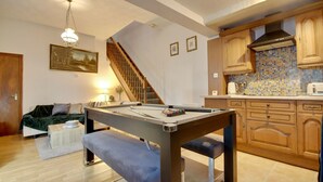 Un salon chaleureux avec une table de billard, un escalier et un coin cuisine doté de meubles en bois et d’un dosseret carrelé.