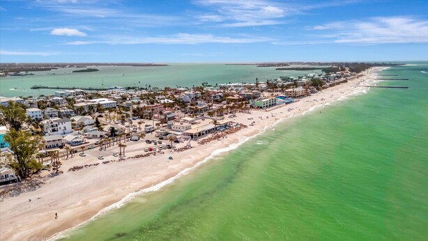 Vista aérea de un pueblo costero con propiedades frente a la playa, un muelle y una vista despejada del océano.