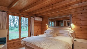 Ein Schlafzimmer einer Holzhütte mit einem großen Bett, einem Nachttisch, einem Stuhl und einem Fenster mit Vorhängen.