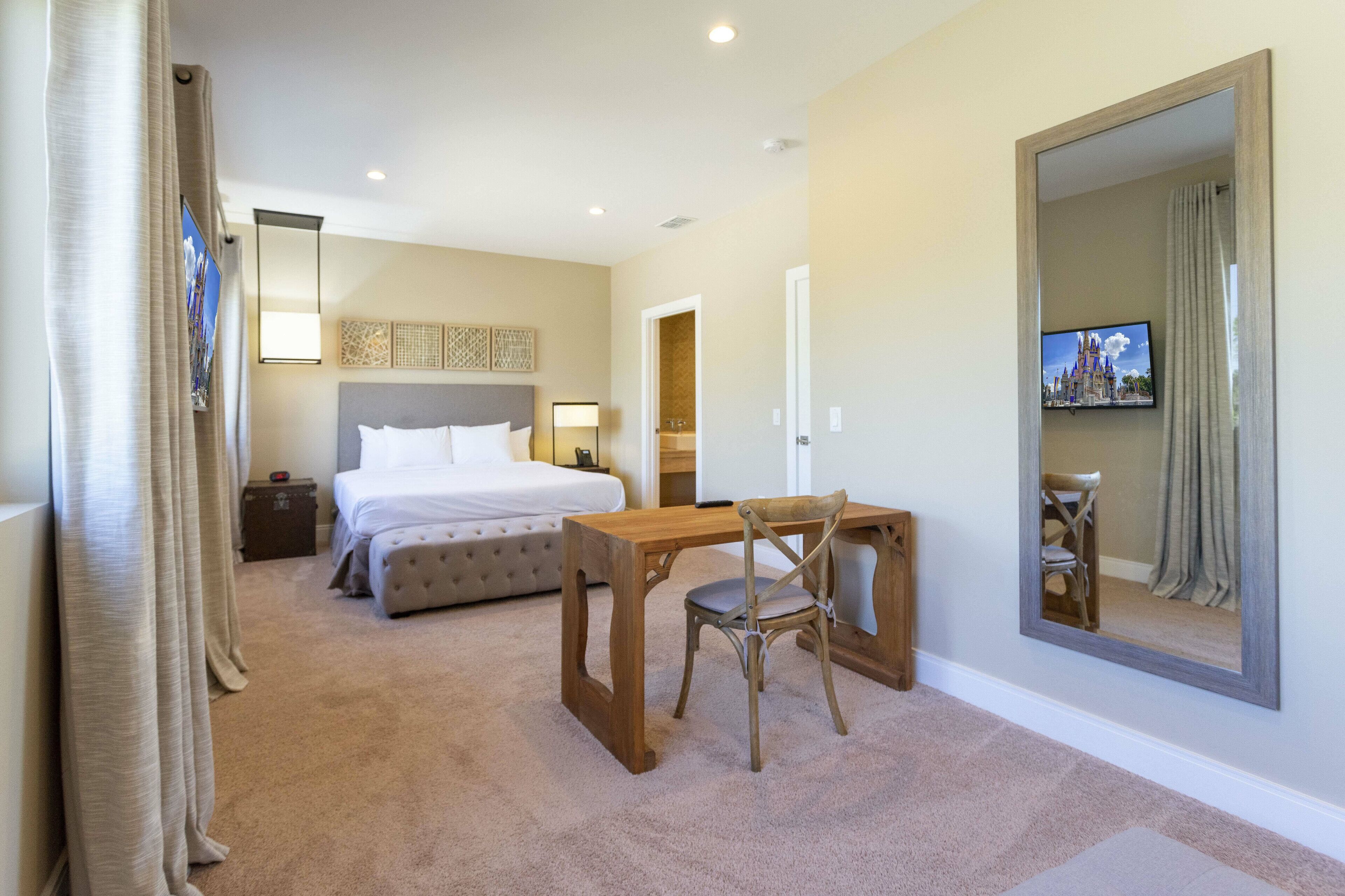 Une chambre d’hôtel avec un lit, un bureau en bois, une chaise, un grand miroir et un téléviseur fixé au mur.