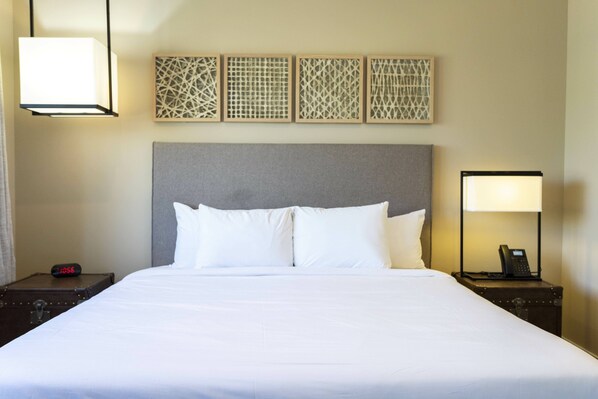 A hotel room with a large bed, a nightstand with a lamp and phone, and a wall clock.