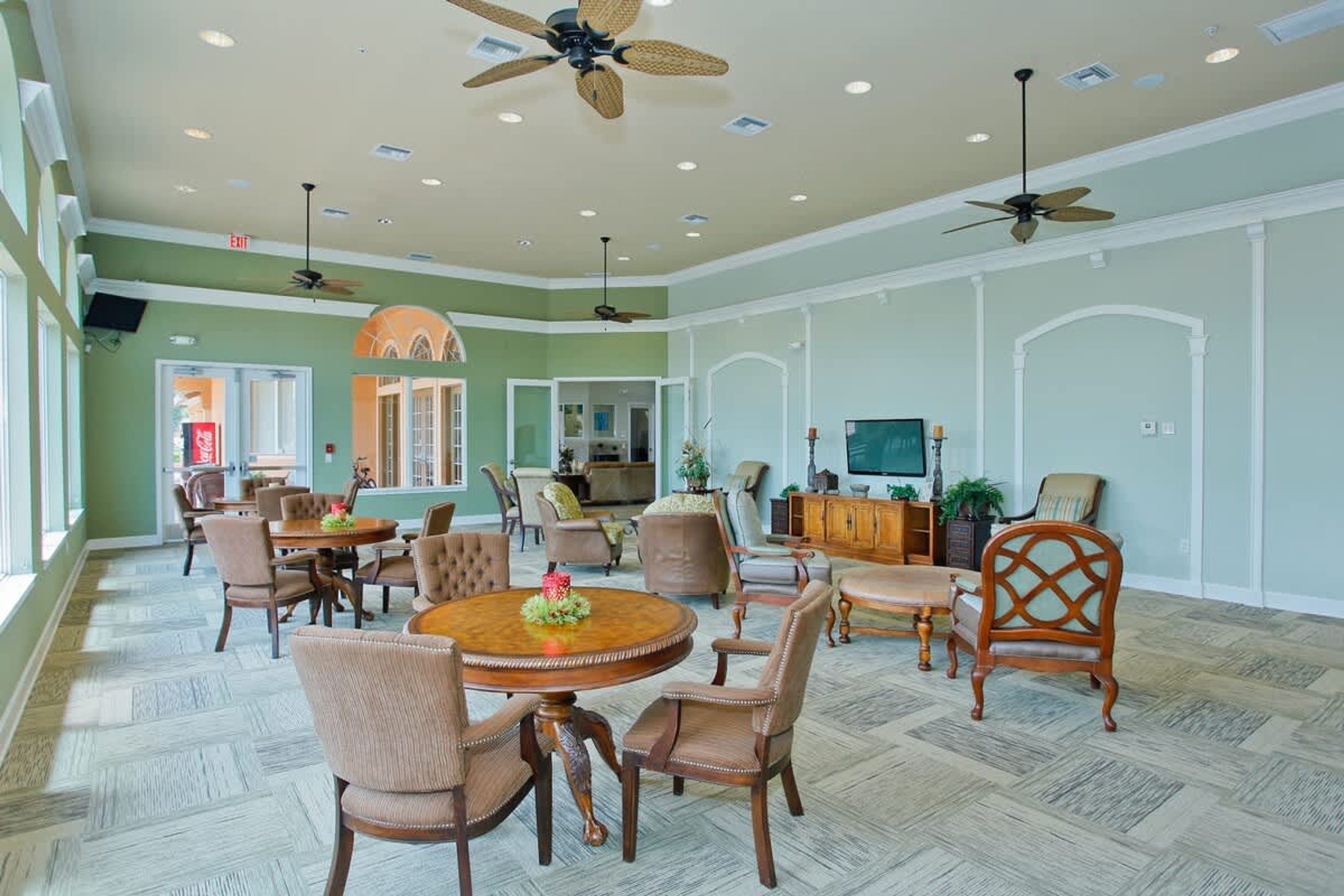 A spacious dining area with round tables and chairs, ceiling fans, and a television.