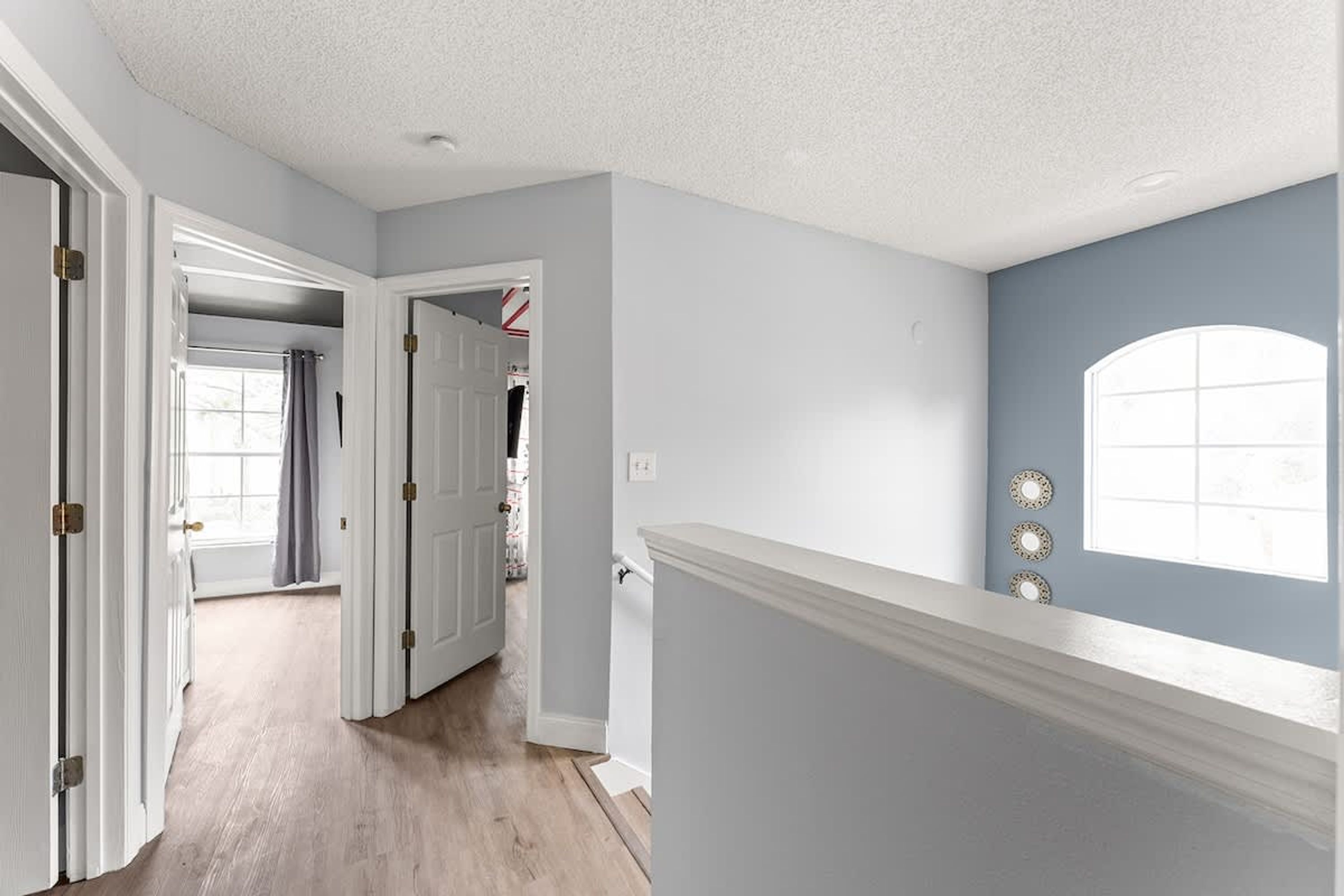 A hallway with white walls, a wooden floor, and a door leading to another room.