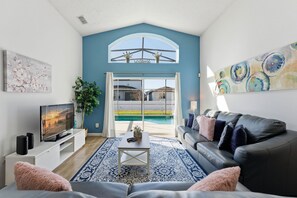 A modern living room with a blue accent wall, a large window, a pool view, a leather sofa, and a flat-screen TV.