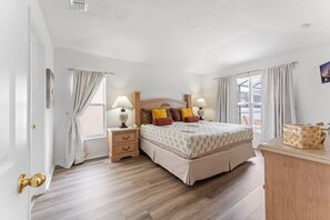 A bedroom with a large bed, bedside tables with lamps, a wooden dresser, and a window with curtains.