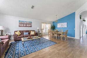 A living room with a brown leather sofa, a blue patterned rug, a dining area with wooden chairs, and a blue accent wall.