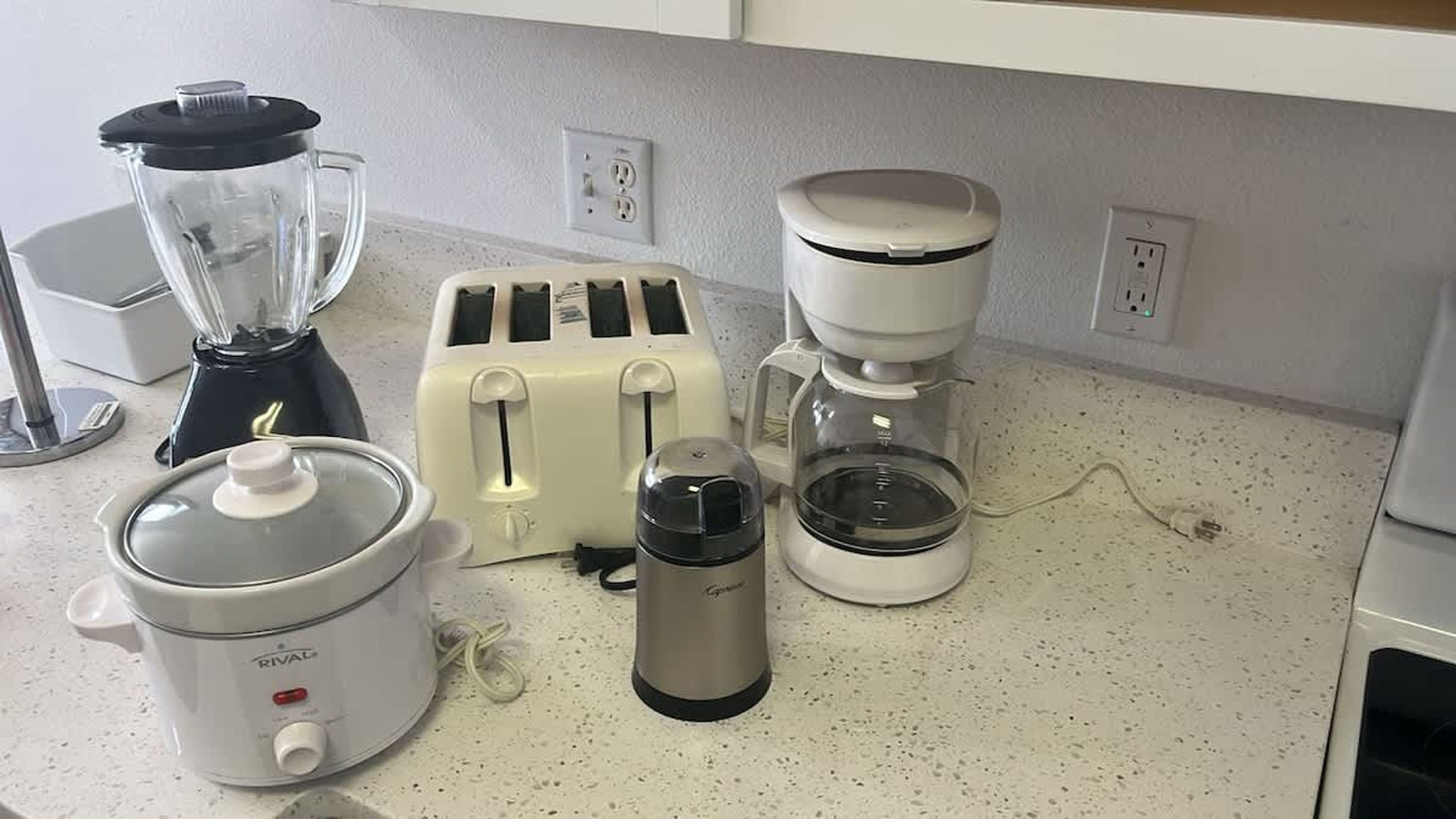 En køkkenbordplade med en blender, en brødrister, en kaffemaskine og en slow cooker.