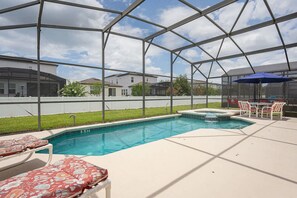 A covered outdoor swimming pool with lounge chairs and a hot tub.
