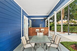 Une terrasse couverte avec une table et des chaises, un comptoir en bois et une vue sur l’extérieur.