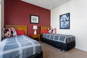Habitación de hotel con dos camas, paredes rojas y ropa de cama temática de Mickey Mouse.