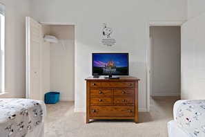 A bedroom with a wooden dresser, a television displaying a Disney castle, and a Snoopy wall decal.