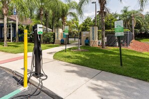 An electric vehicle charging station in a landscaped area with palm trees and a gated entrance. - Welcoming 4 BR Sleeps 10 Guests Wl2901 (Kissimmee)