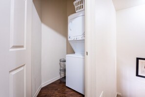 Un lavadero con lavadora y secadora apiladas, un tendedero de metal y una puerta que da a otra habitación.